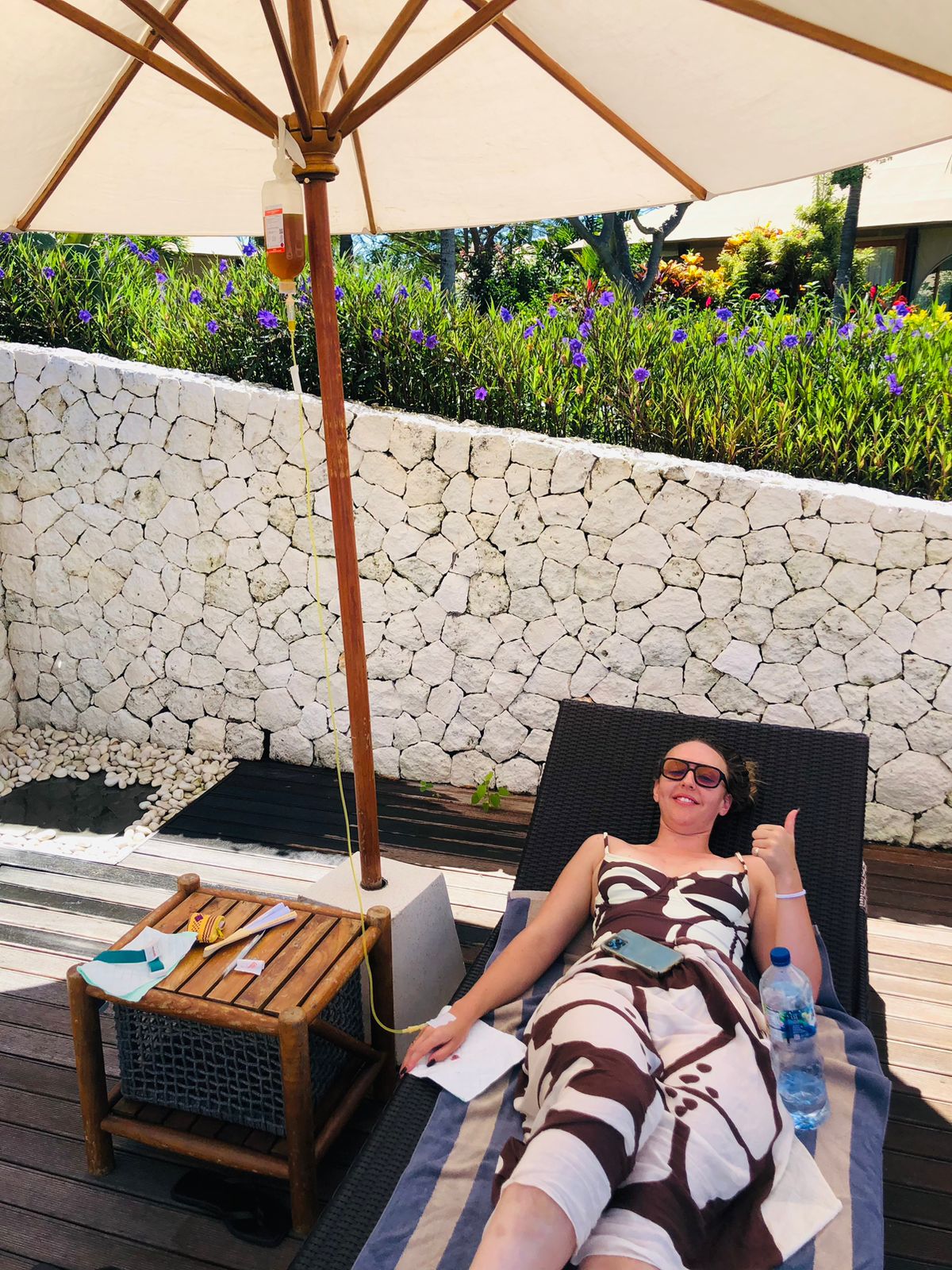 Woman relaxing on a lounge chair under an umbrella while receiving a mobile IV drip therapy.